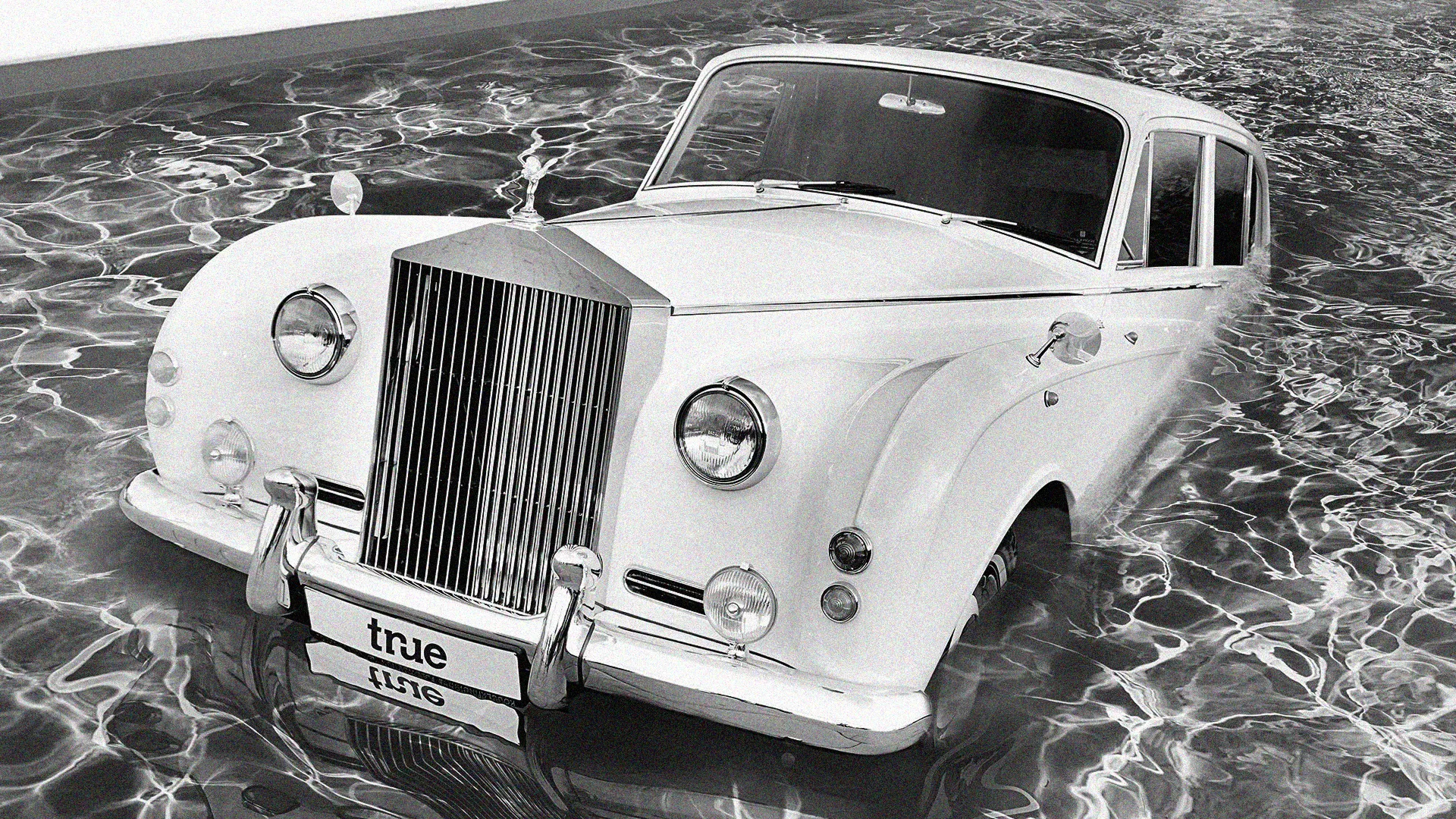 A white Rolls-Royce with a True number plate reflected in water