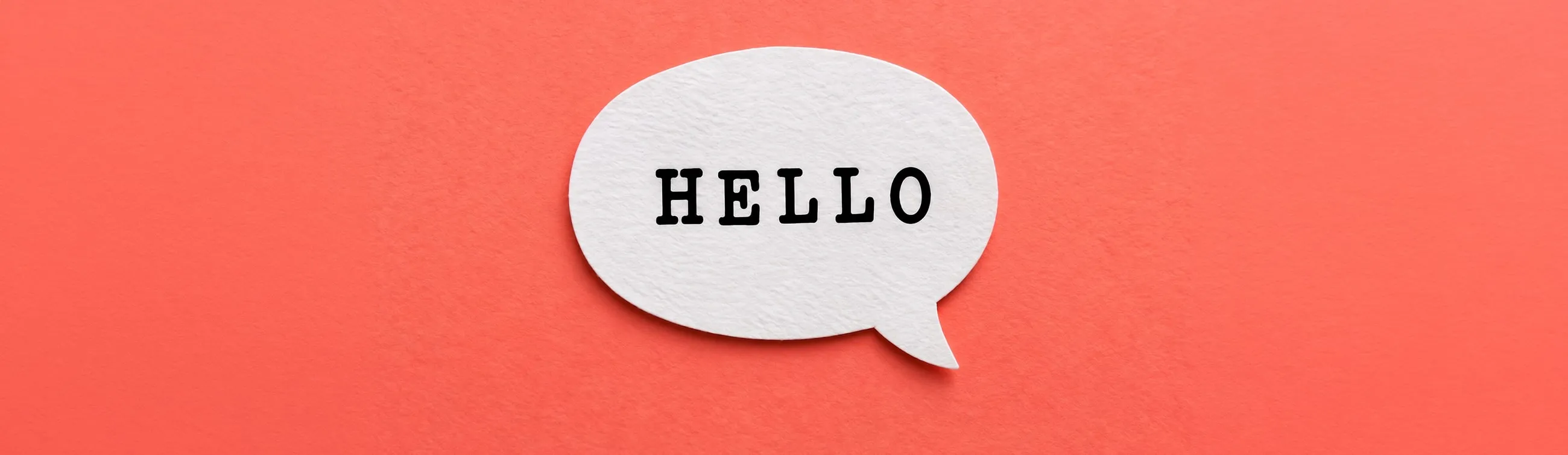A white paper speech bubble with the word HELLO typed on it, on a coral red background